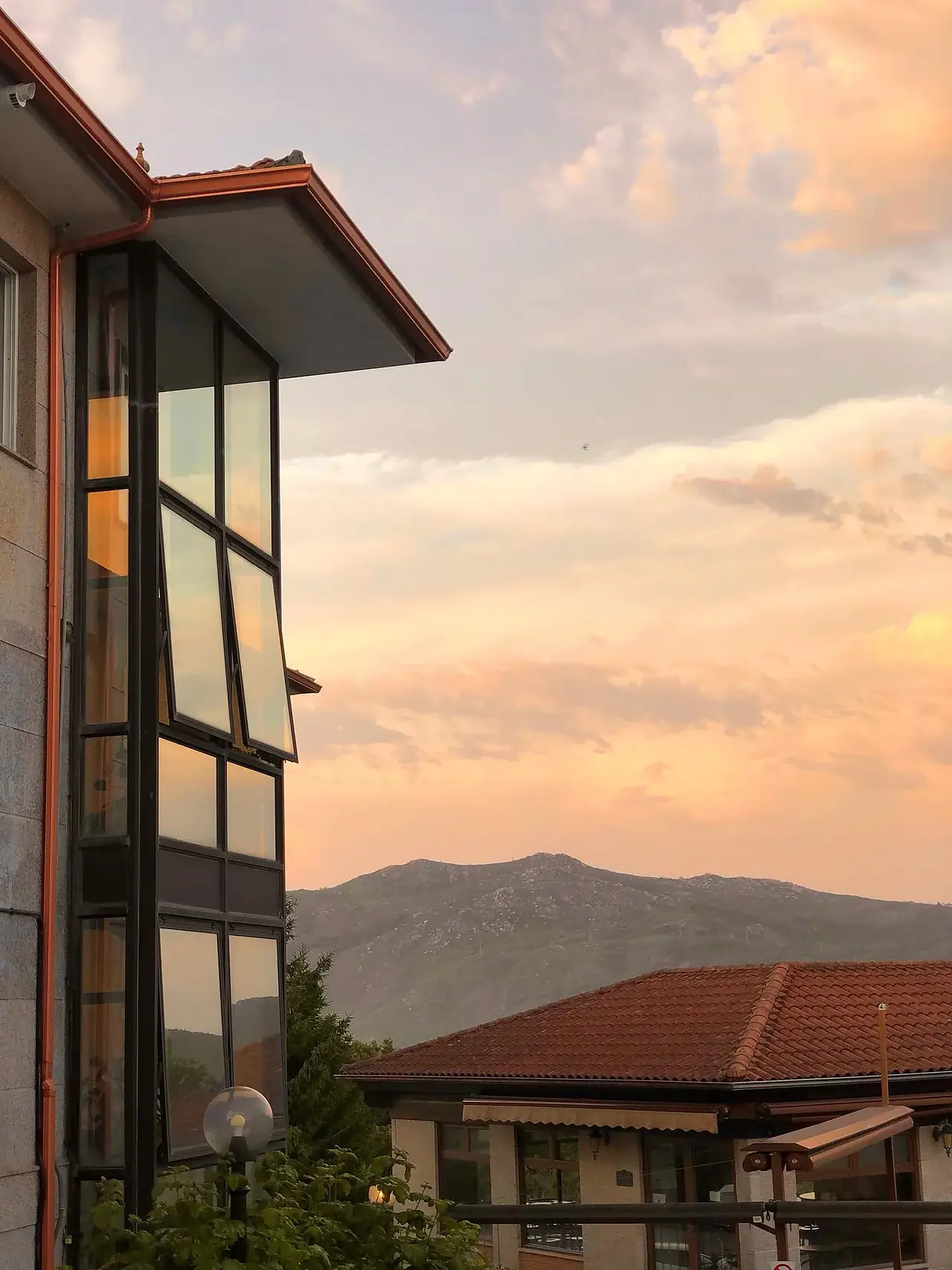 La fachada acristalada del Hotel Restaurante El Bosque en Mos al atardecer, con las montañas al fondo