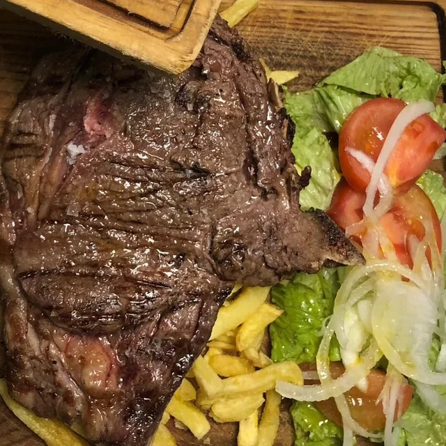 Carne a la parrilla en tabla de madera con ensalada y patatas fritas en el restaurante El Bosque, en Mos