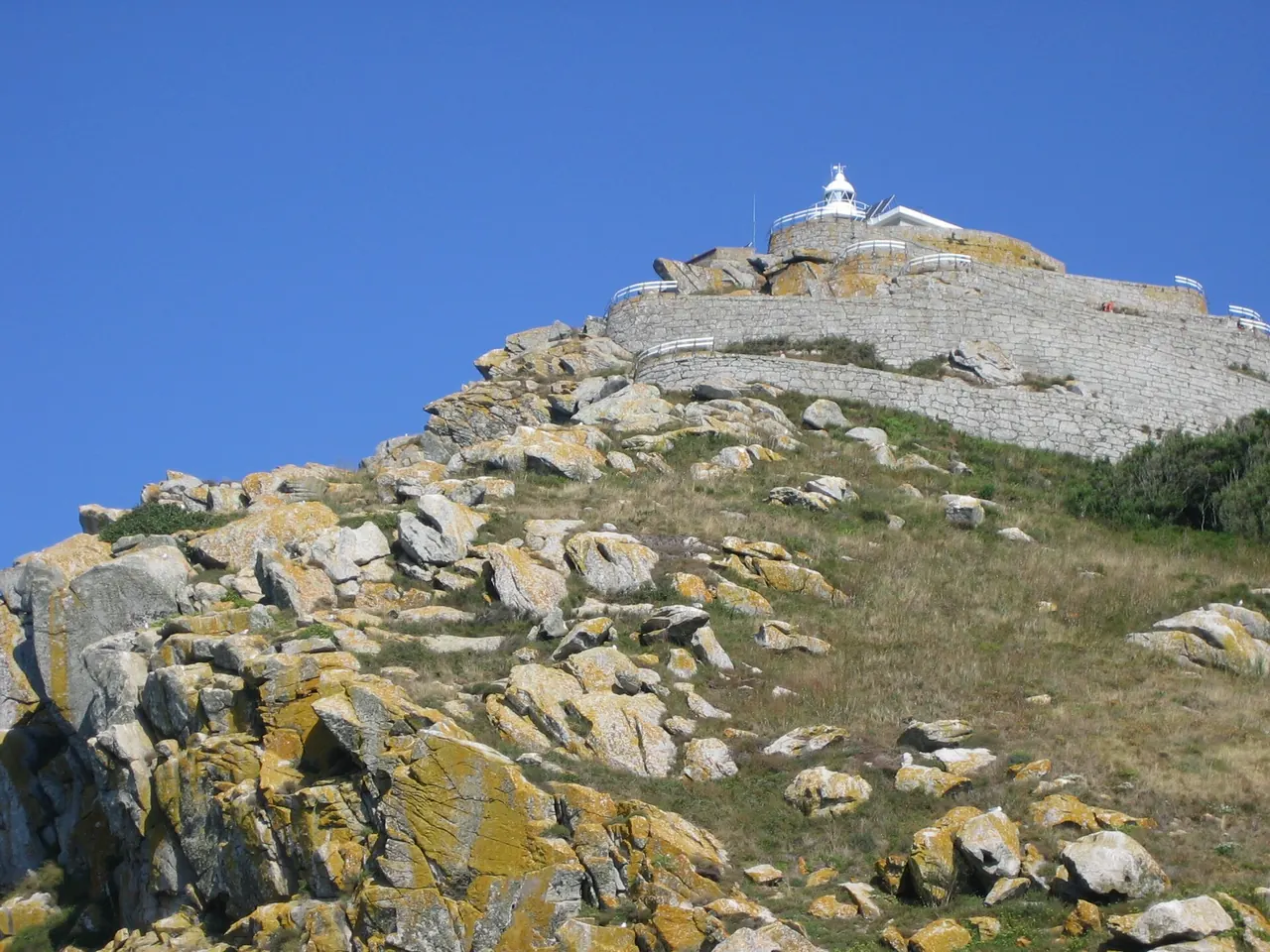Faro de Cíes en lo alto del Monte Faro, con su muro de piedra sobre rocas de granito y cielo azul