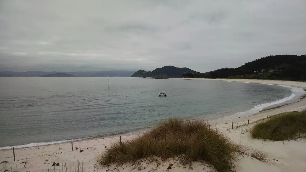 Playa de Rodas vista desde las dunas en un día nublado, con la ensenada en calma y los montes de Cíes al fondo