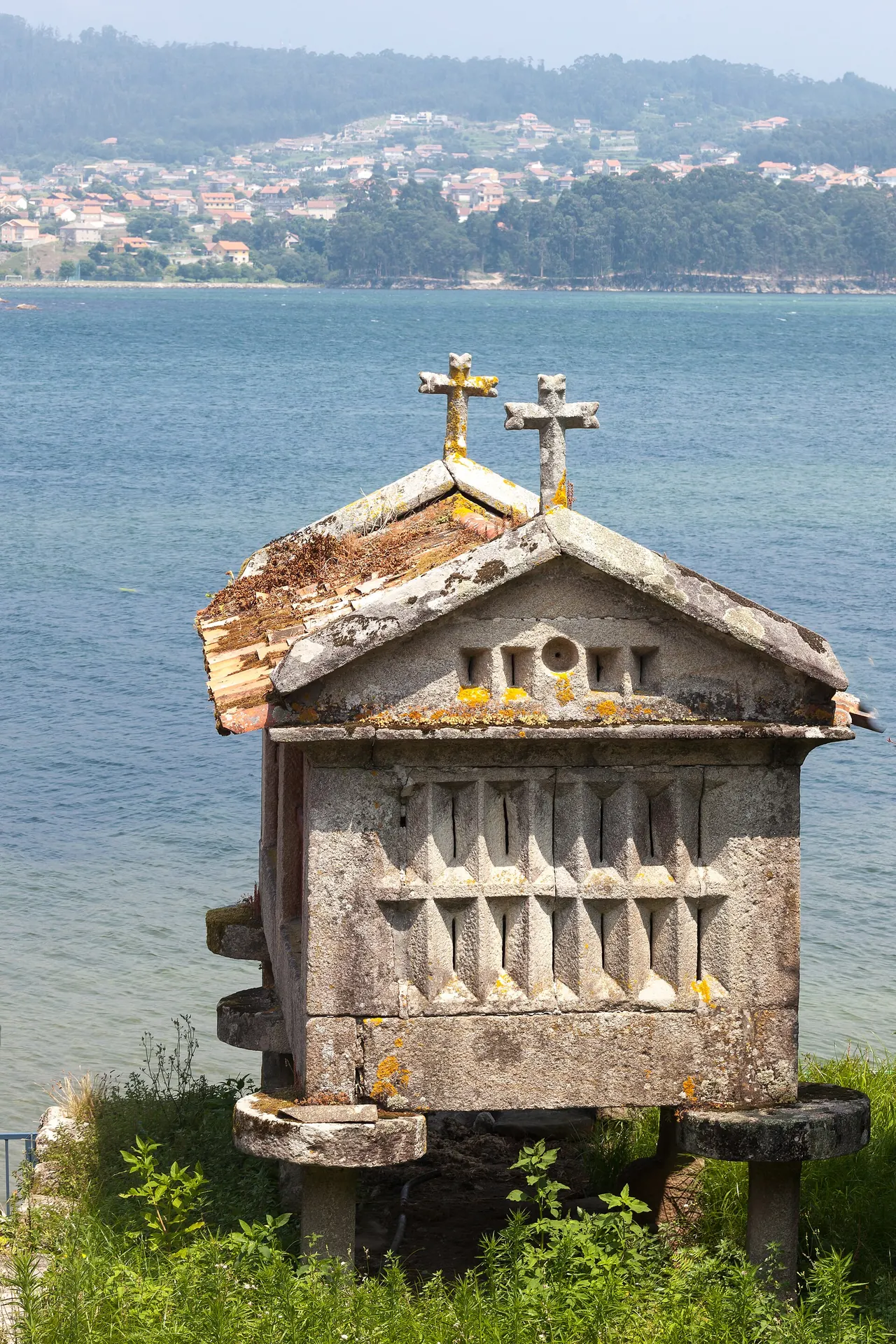 Hórreo de piedra con dos cruces en el tejado, en Combarro, con la ría de Pontevedra y la otra orilla al fondo