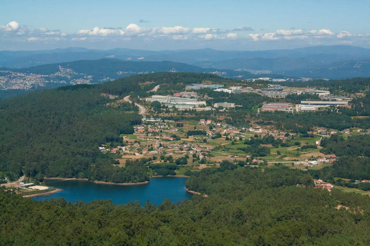Vista desde lo alto del Monte Galiñeiro: pinares, un embalse azul, aldeas y naves industriales, con montes al fondo