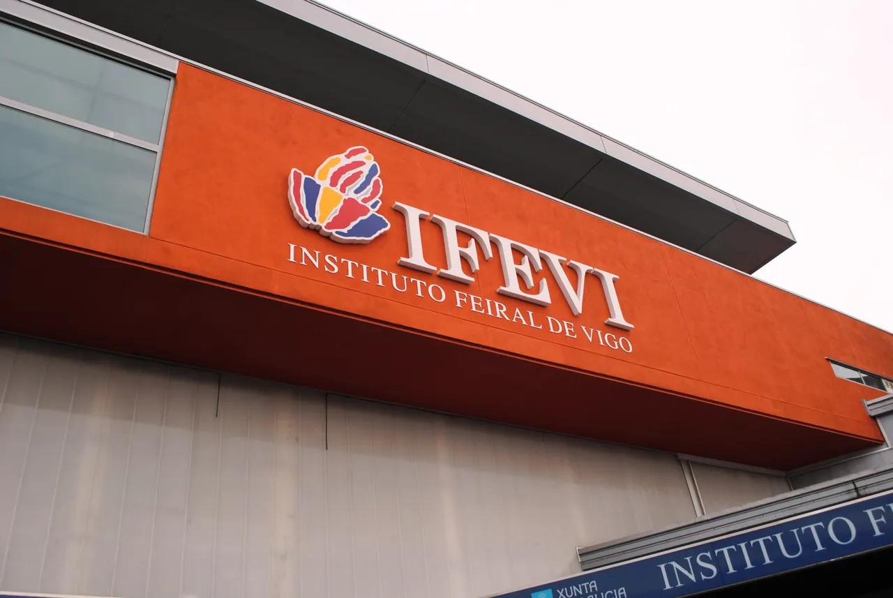 Rótulo «IFEVI Instituto Feiral de Vigo» con el logotipo de colores sobre la fachada naranja del recinto ferial, en Vigo