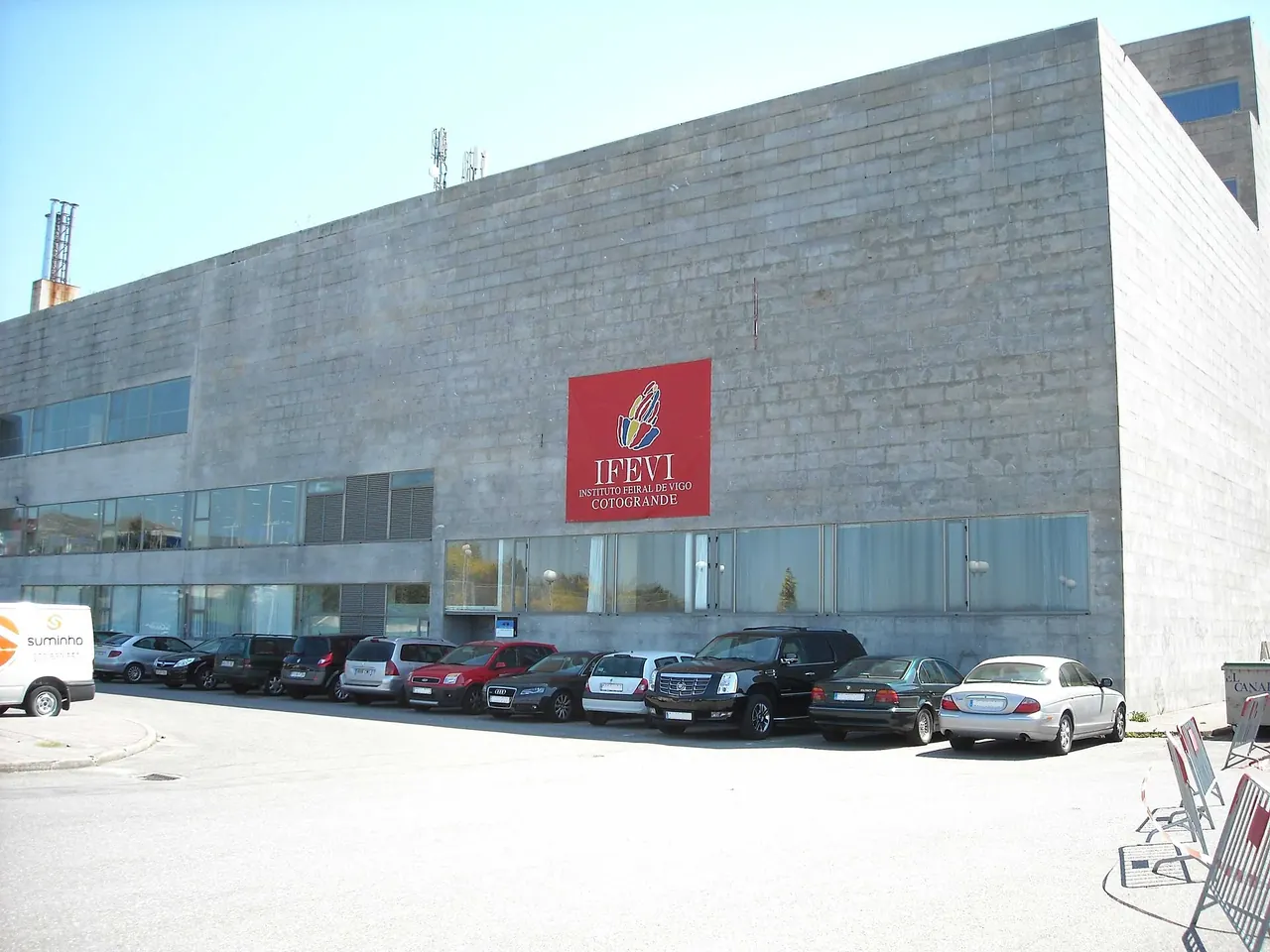 Fachada gris del IFEVI, en Vigo, con el rótulo rojo «IFEVI Instituto Feiral de Vigo Cotogrande» y coches aparcados delante