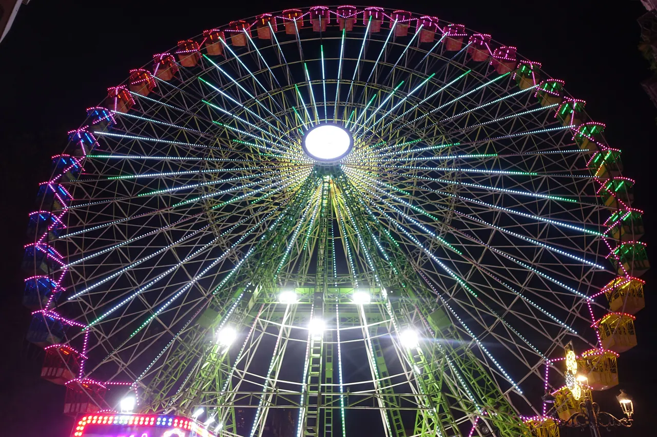 Noria iluminada de noche en Vigo durante la Navidad de 2024, con luces verdes, blancas y rosas en los radios y las cabinas