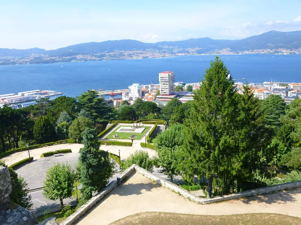 Jardines y caminos del Monte do Castro, con los edificios de Vigo, el puerto y la ría azul detrás
