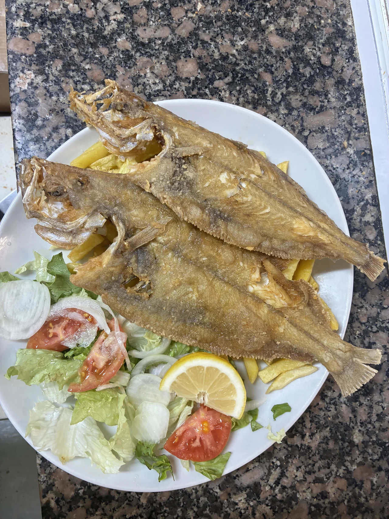 Plato con dos pescados enteros, patatas, ensalada y limón